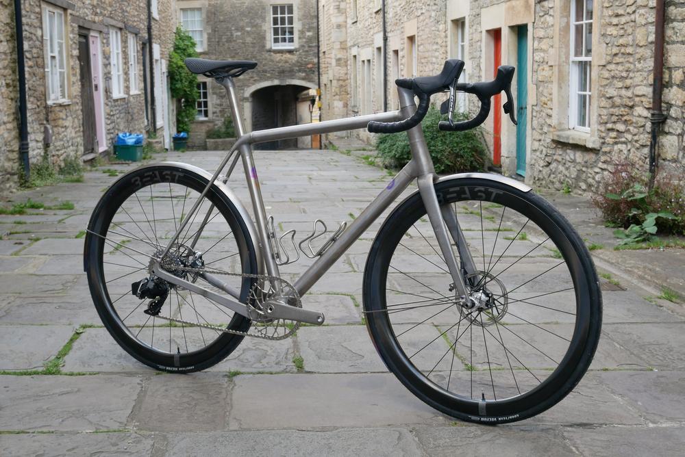A silver titanium bicycle is parked on a stone street.