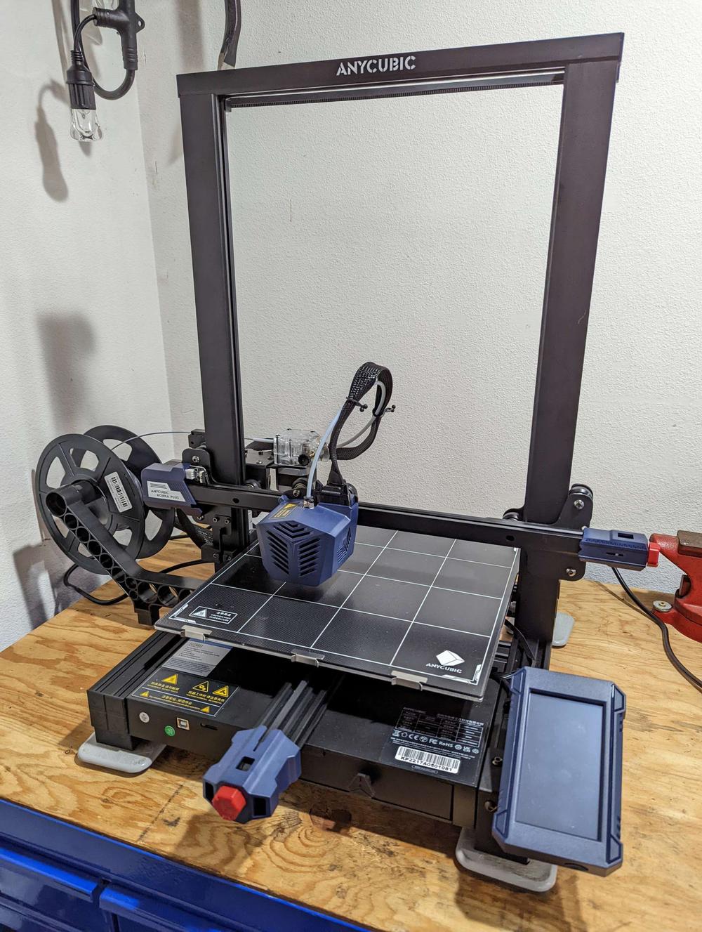 A black and blue Anycubic Mega X 3D printer is printing a blue object on a glass bed.