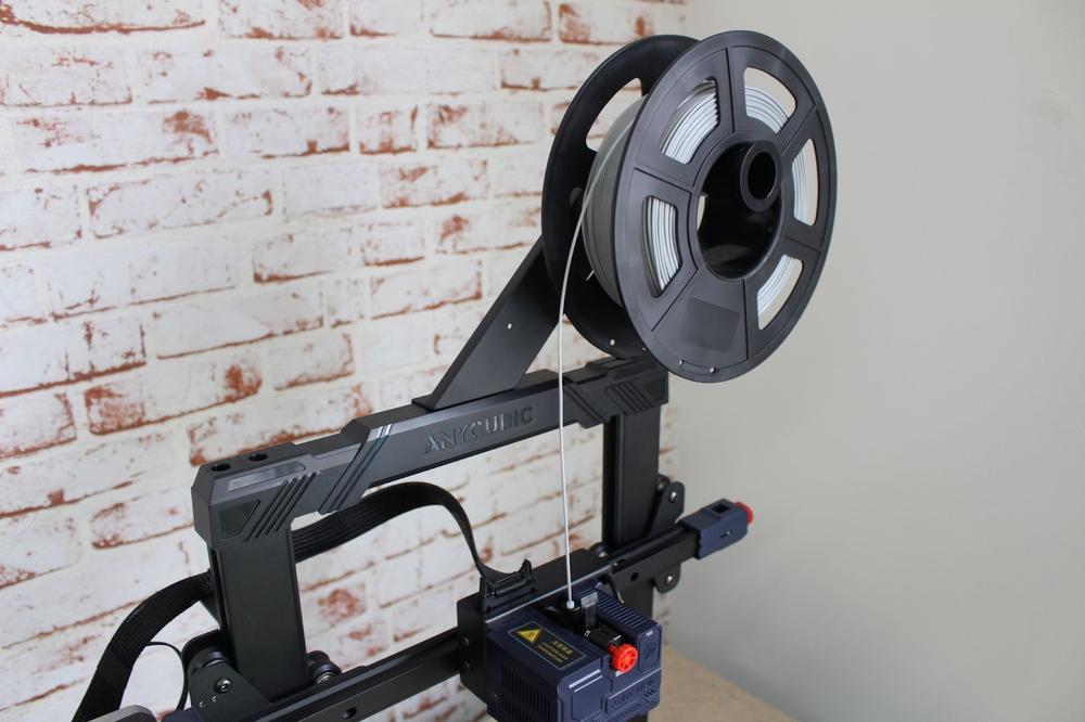 A spool of white filament is loaded onto a black and red 3D printer.