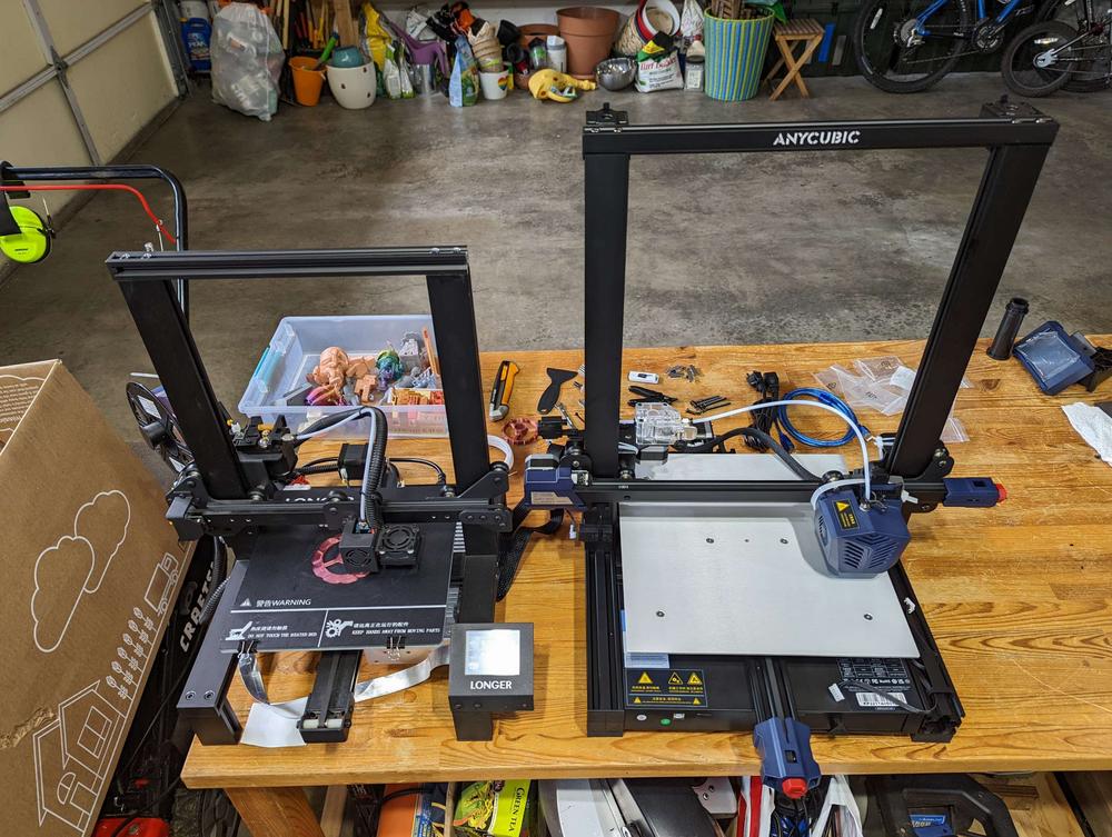 Two black resin 3D printers are sitting on a table in a garage.