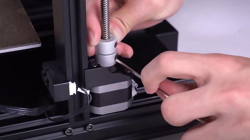 A person is using an Allen key to tighten a screw on a 3D printer.