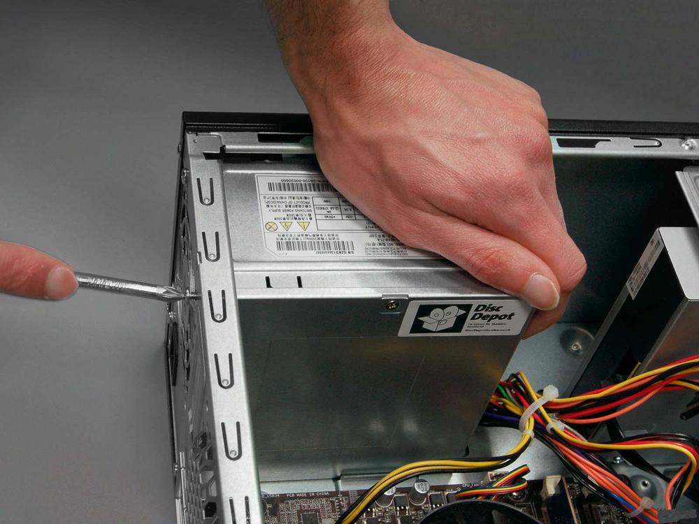 A hand is using a screwdriver to remove the side panel of a computer case.