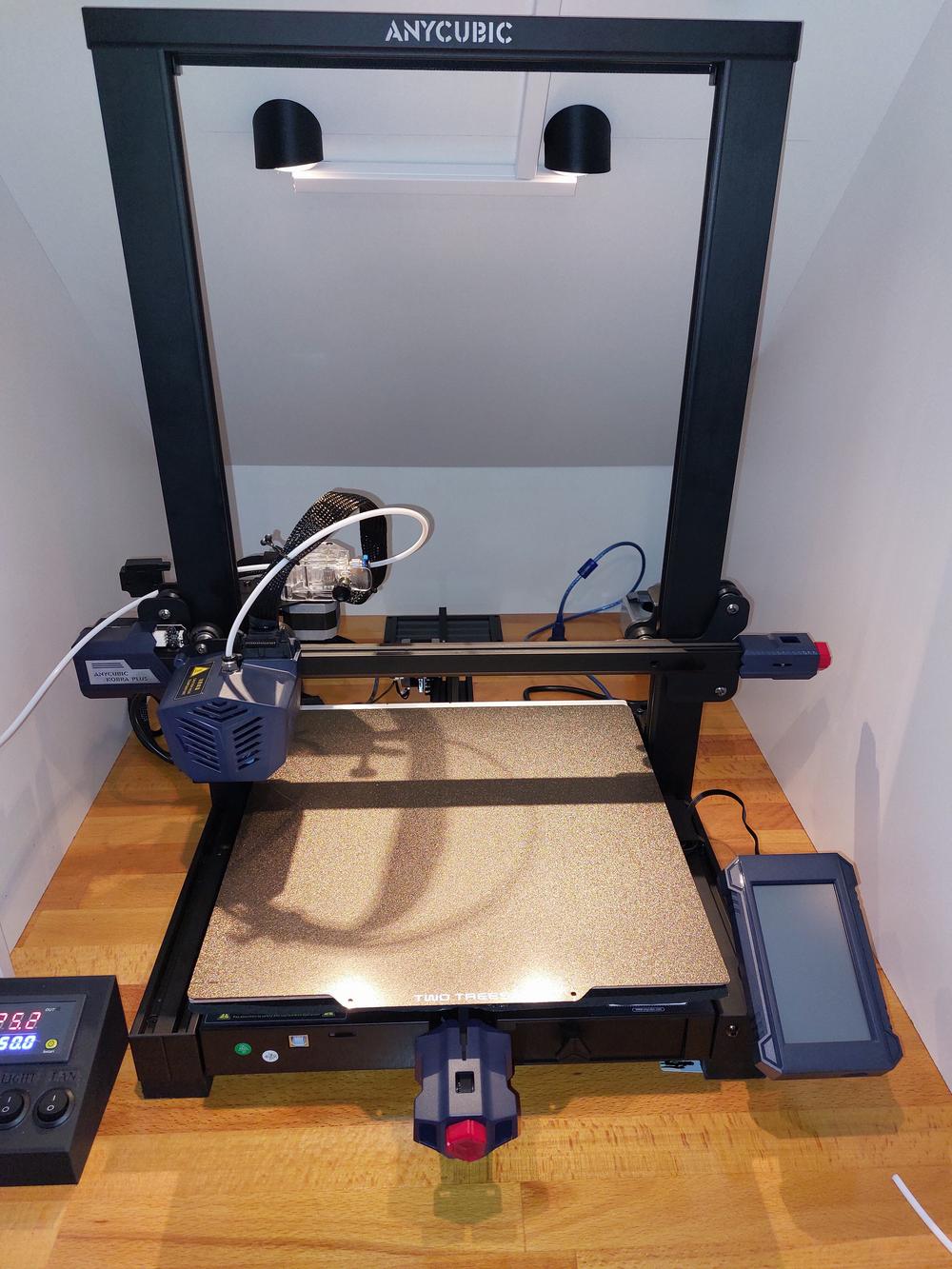 A black and grey 3D printer with a build platform, control panel, and two LED lights.
