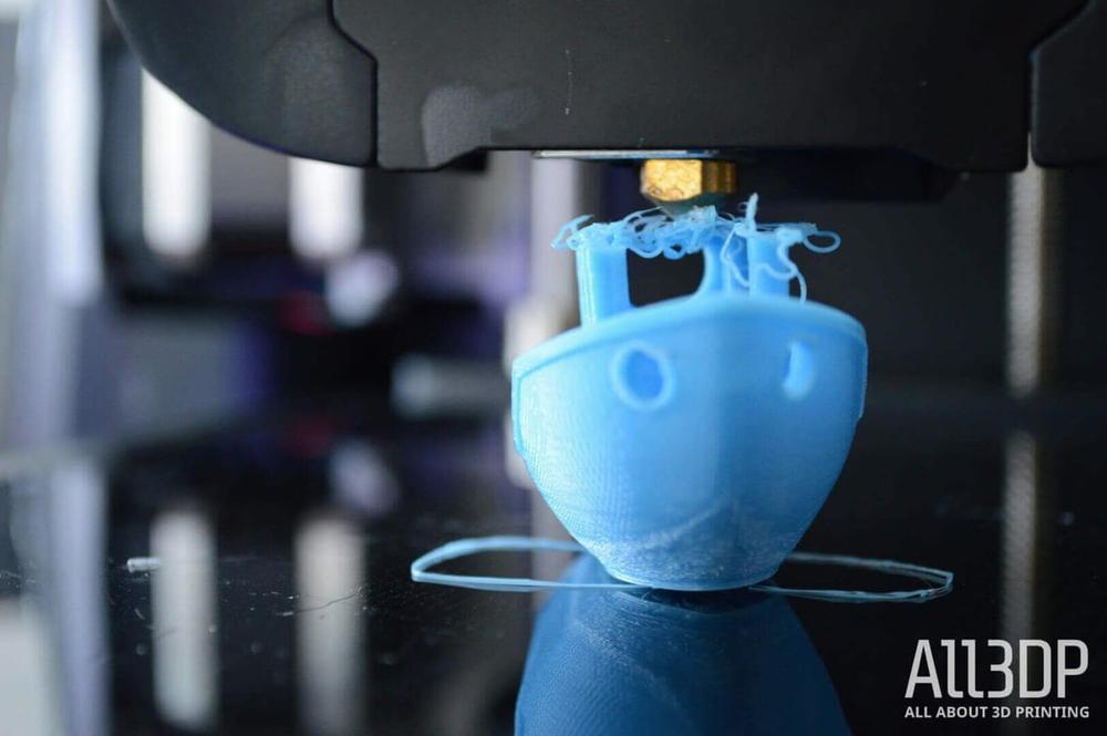 A 3D printer is printing a blue plastic boat.